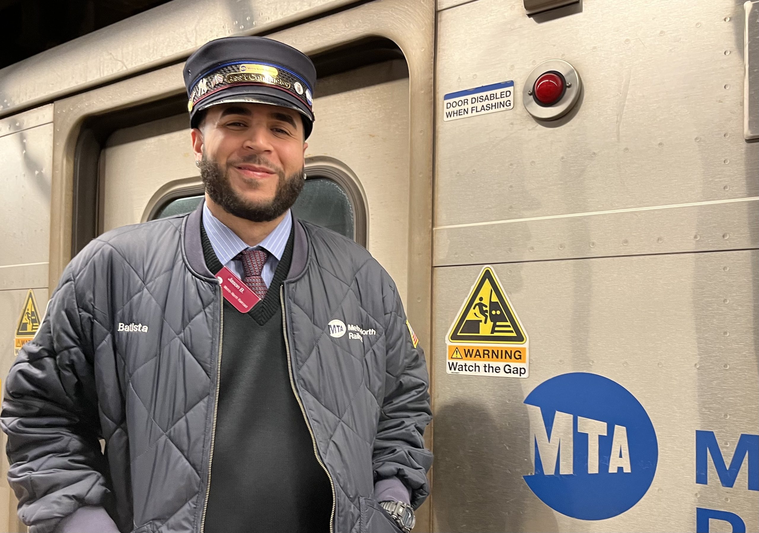 A man in a conductor's uniform stands in front of a Metro North train.