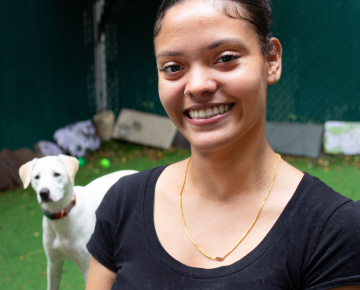 Young woman in a black shirt standing in front of a dog daycare outdoor exercise area.