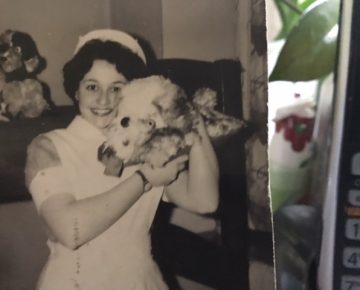 Black and white image of Enid Zwirn in nurse uniform holding up a dog on the right shoulder