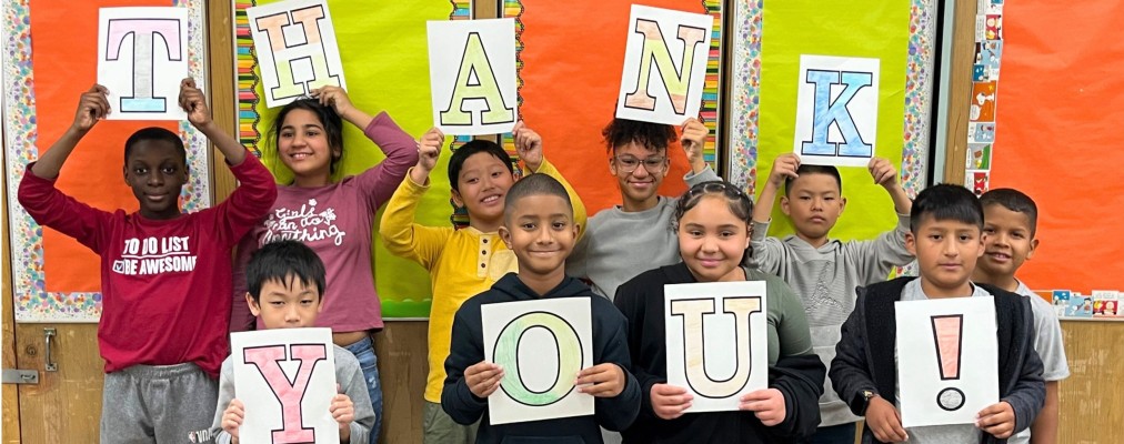 Kids lined up in two lines each holding up a letter sign that forms THANK YOU.