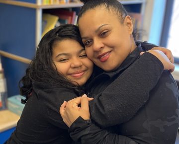 A child wraps her arms around her mother in a big hug.