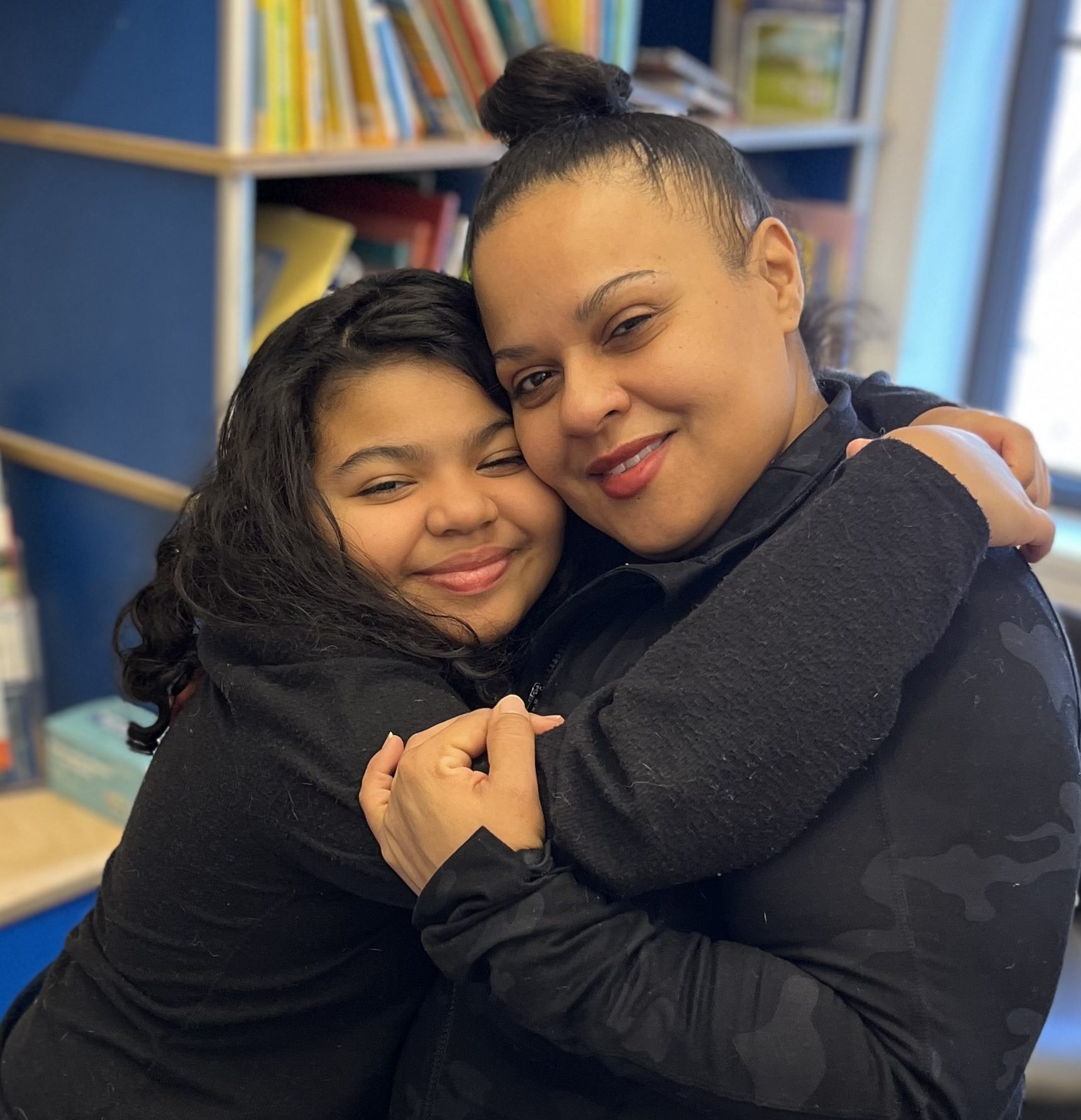 A child wraps her arms around her mother in a big hug.